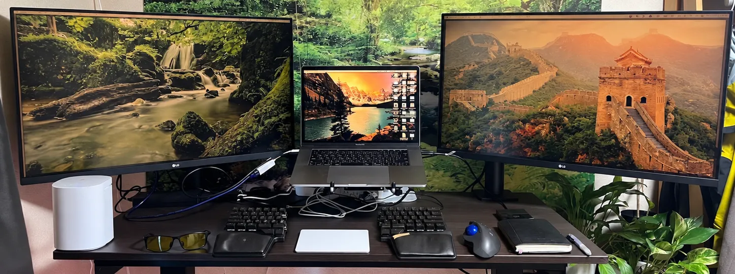 2枚のLGモニターの間にMacBookを置き、手前に分割キーボードとトラックボールマウスを並べたスタンディングデスク